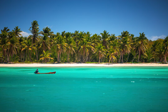 Small boat in turquoise water near tropical palm beach in Saona Island, Dominican Republic