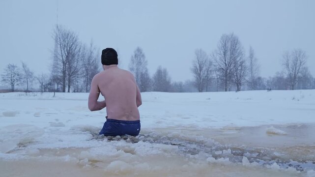 Slow motion cold plunge in freezing water during snowfall and strong winter wind