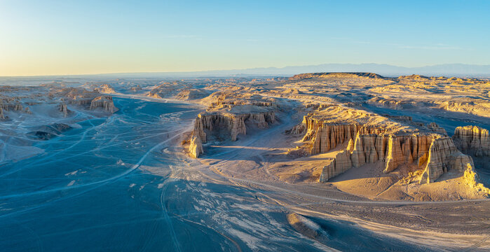 Aerial view of unique geological yardang landforms with dry clay cliffs in a vast arid desert at sunset, Dahaidao, Xinjiang, China