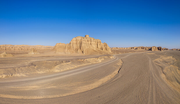 An empty desert road winding through yardang landforms under a clear blue sky, Dahaidao, Xinjiang, China