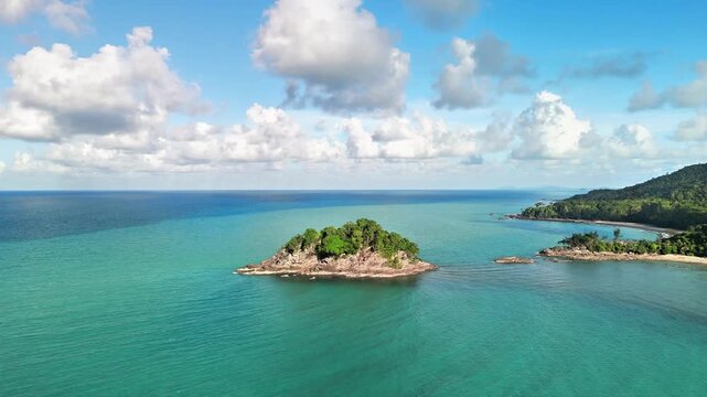 Aerial drone view of a secluded tropical island near a hidden beach surrounded by turquoise ocean granite shoreline and dramatic cloudscape above