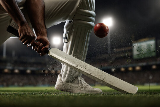 Cricket batter striking red ball near ground with dirt and grass flying under stadium lights. Concept of batting technique, match intensity, tournament promotion, sports advertising and branding.