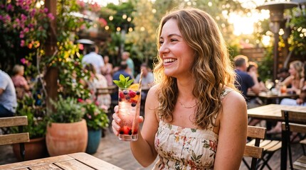Fototapeta premium Smiling woman enjoying a refreshing berry cocktail at an outdoor garden patio during golden hour sunset, celebrating summer joy and relaxation.