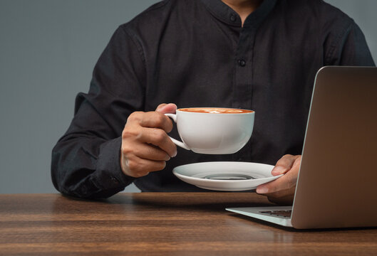Person taking a coffee break beside laptop at desk