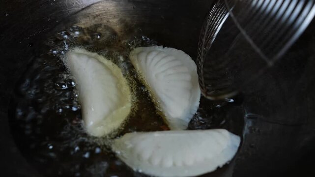 Three dumplings frying in hot oil in a pan, with a strainer spoon beside them, showing a close-up of home cooking and crispy food preparation