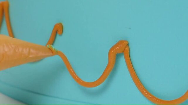 Piping orange frosting loops onto the side of a blue cake close-up