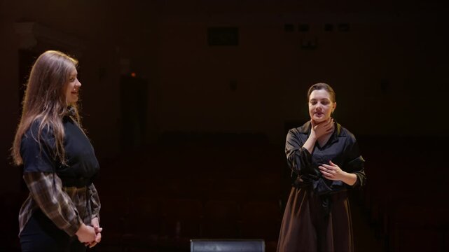 Acting coach guiding theater students on a dimly lit stage during rehearsal, emphasizing performance techniques, communication, and expressive body language in an empty auditorium