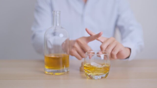 Man making stop hand gesture to refuse a glass of whiskey, Healthy man say no to alcohol drink, stop alcoholism and addiction concept. Responsible man reject a drink before driving and quit booze