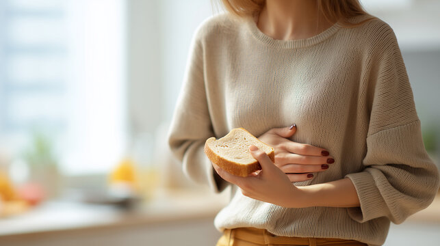 Woman holding a slice of bread while experiencing stomach discomfort. Gluten intolerance, celiac disease, digestive problems, food sensitivity and abdominal pain concept with copy space.