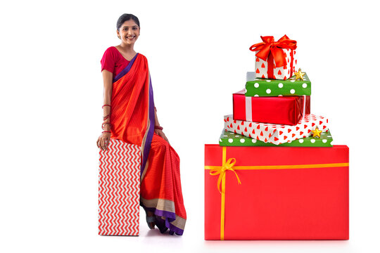 Cheerful woman sitting on gift box against white background
