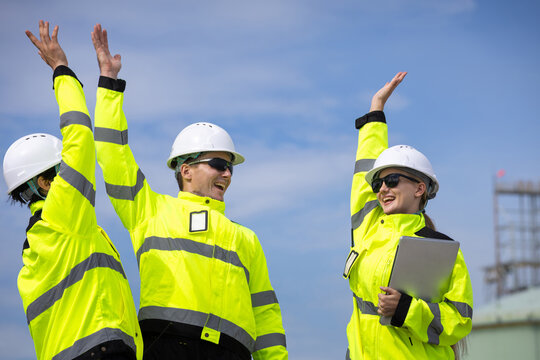 Successful engineering team celebrating achievement at construction site, Happy construction workers with hardhat cheering for success, industrial team celebrating project completion at refinery