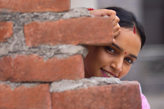 Close-up portrait of young woman peeking from behind brick wall