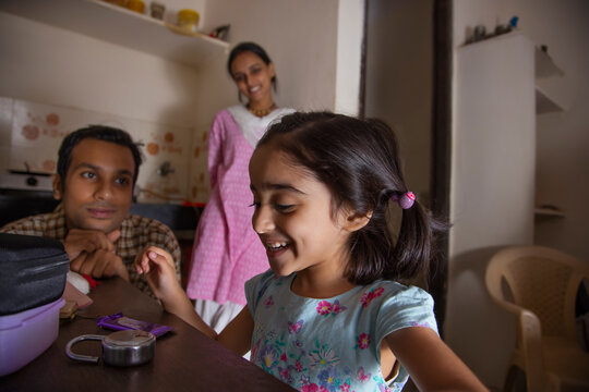 Happy little girl looking at chocolate and her parent standing beside in the kitchen 