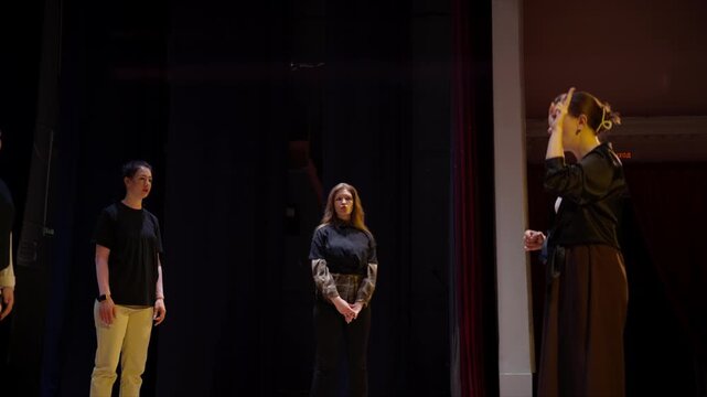 Theater director instructing performers on stage under warm spotlight during dramatic rehearsal, guiding ensemble actors through expressive movement and dialogue