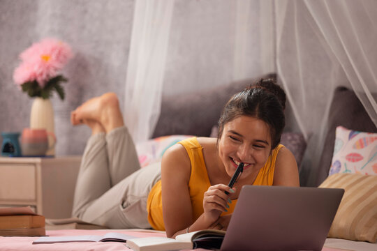 Teenage girl lying on bed and studying with laptop