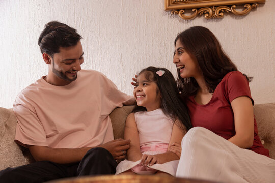 Happy young couple with their daughter sitting together on sofa at home