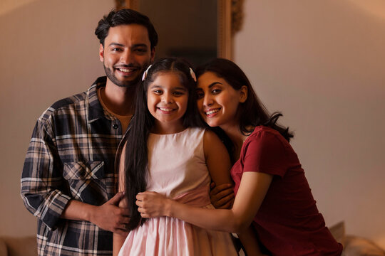 Portrait of happy couple with their girl child looking at camera at home