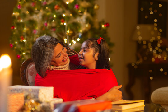Little girl sitting on her grandmother's lap in the living room covered with a red sheet