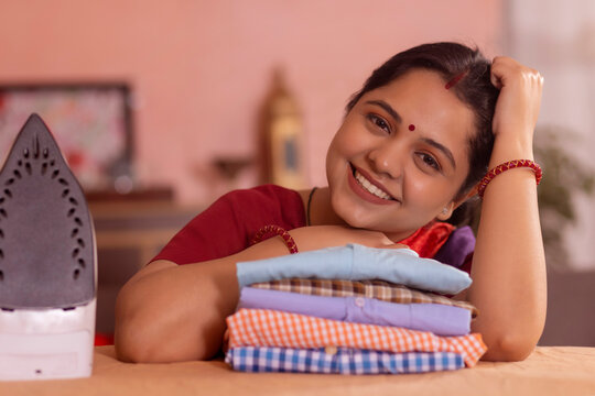 Close-up portrait of a happy woman looking at camera with resting her chin on ironed shirts