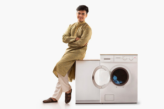 Young man in traditional outfit sitting near washing machine