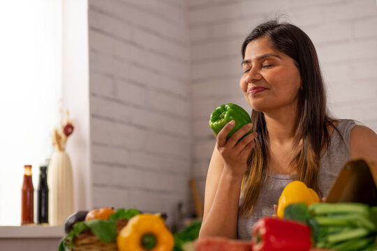 Woman holding a fresh green bell pepper in kitchen