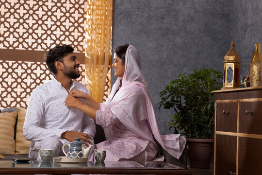 Muslim woman buttoning her husband's shirt in living room