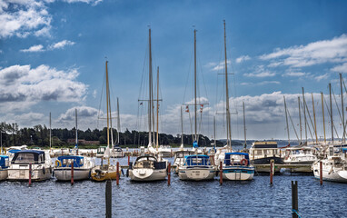 Fototapeta premium Luxury yachts docked at marina in scenic coastal town. Elegant sailboats and motorboats moored by vibrant harbor with dramatic sky backdrop, Falsled, Denmark