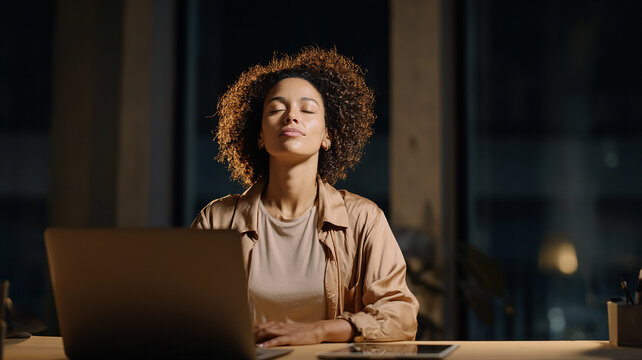 Young businesswoman practicing mindfulness meditation during a late night work break with laptop in a modern office for workplace mental wellbeing