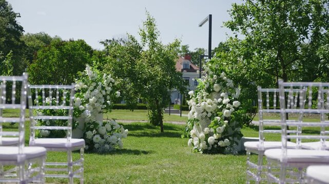 Wedding ceremony scene featuring elegant floral arrangements and transparent chairs set up in a lush outdoor garden space