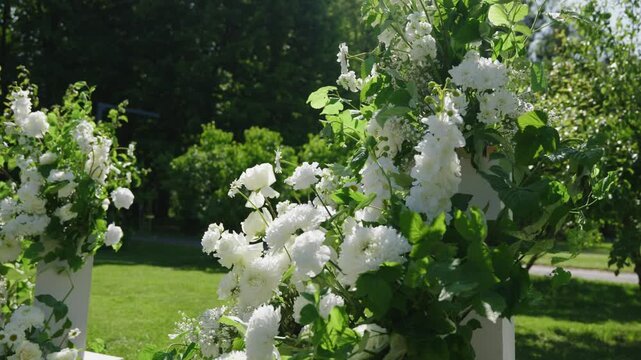 Beautiful white floral arrangements with greenery create a stunning backdrop in a garden, enhancing the romantic atmosphere for a wedding ceremony