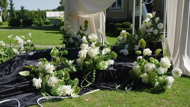 Wedding ceremony setup featuring lush white floral arrangements and elegant drapery on a sunny day in a garden setting