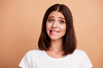Fototapeta premium Brunette young woman in white tshirt making a funny awkward expression against beige background