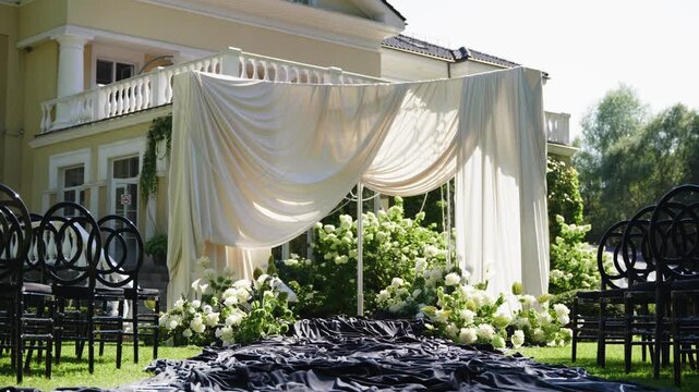 Beautiful wedding ceremony space featuring draped fabric and lush floral arrangements, set in a garden with a charming house in the background