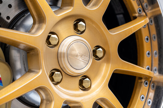 Macro close up of a luxury custom gold alloy wheel rim and tire with a BMW M brake caliper, drilled brake disc rotor. Macro close up of a custom gold SSR alloy wheel rim center cap with bolts. 
