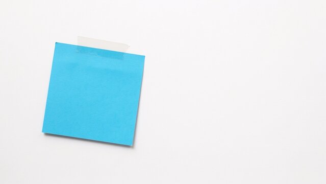 Bright blue square sticky note taped to a plain white surface