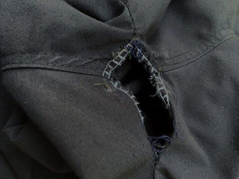 Close up of a ripped hole on the seam of black fabric pants.