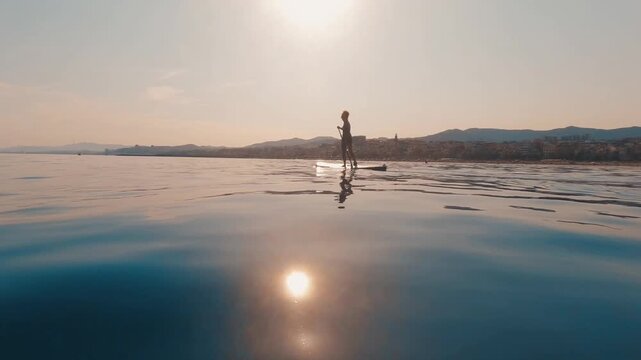 V&iacute;deo de una persona practicando paddle surf sobre mar en calma, con reflejo del sol y luz suave.