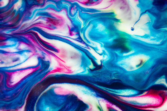 Colors flow and mix in an abstract pattern on a surface in bright shades of blue and pink