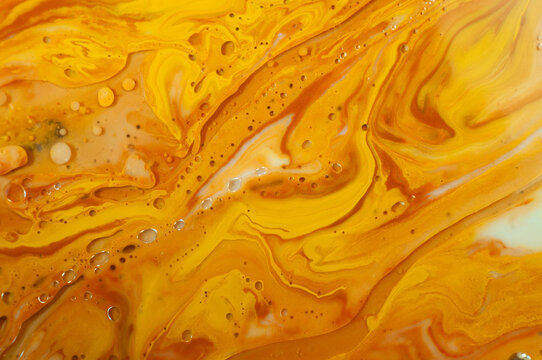 Swirls of bright orange and yellow paint mix together on a flat surface