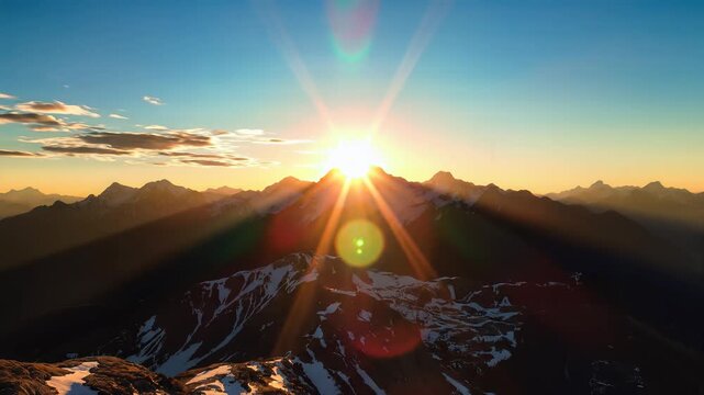 Golden sunrise illuminating rugged snowy mountain peaks with dramatic sky and lens flare