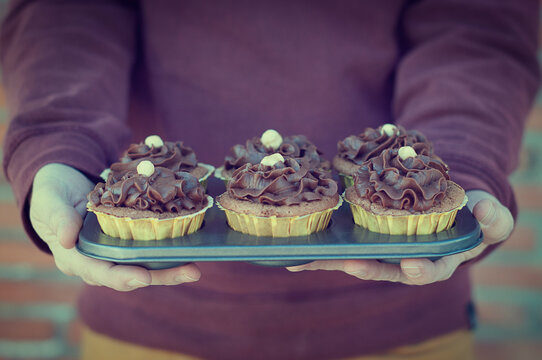 Close-up of a Man holding a freshly baked baking tray of chocolate cupcakes with buttercream icing