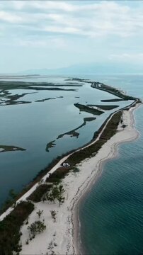 High angle aerial view of a camper van parked on a narrow sandy beach road between the sea and wetlands lagoon