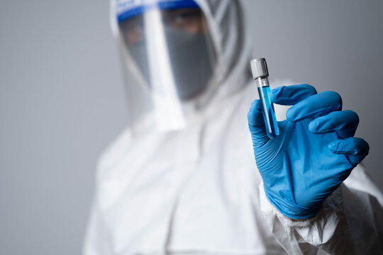 Scientist in protective suit holding laboratory test tube with blue liquid, representing biotechnology research, medical diagnostics, vaccine development and healthcare innovation.