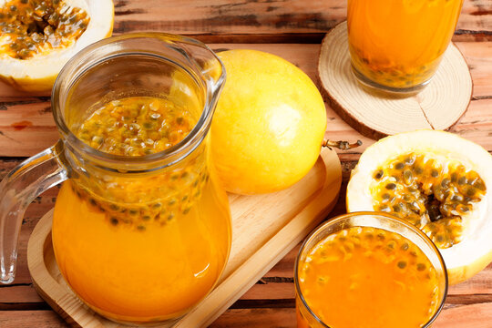 Fresh passion fruit juice served in a glass pitcher, with whole and sliced passion fruits on a rustic wooden table.