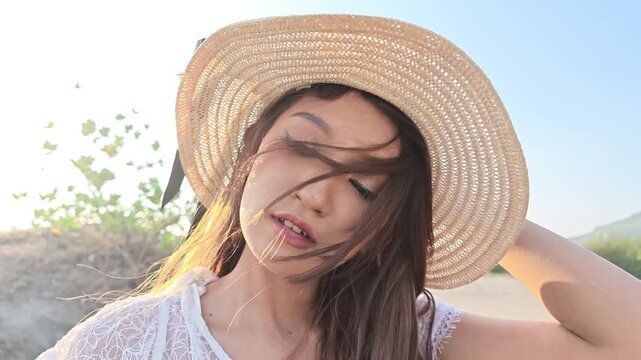 Beautiful Indonesian southeast asian woman in straw hat and white dress posing on sand dunes under sunny sky