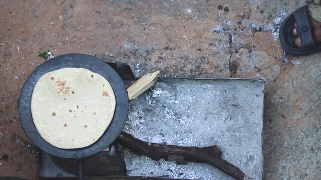 making Indian bread from wheat flour over iron pan in wooden fire.