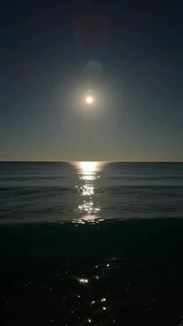 A serene nighttime seascape with the moon shining brightly over calm waters, casting a reflective glow on the surface