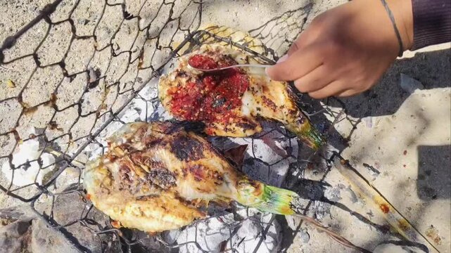 Delicious Ikan Bakar, a traditional Indonesian dish of fish grilled over hot coals, seasoned with a spicy chili sauce. Smoky flavor with a red chili paste consisting chili peppers, garlic, shallots