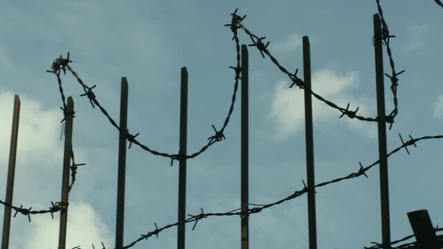 Bird flying past a barbed wire fence against a cloudy sky. Conceptual footage representing freedom, security, restriction, borders.