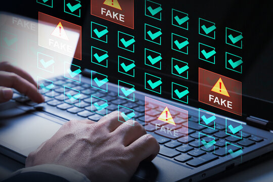 Digital Deception: Close-up on hands typing on a laptop, with a holographic interface displaying numerous checkboxes, some marked FAKE with warning signs.